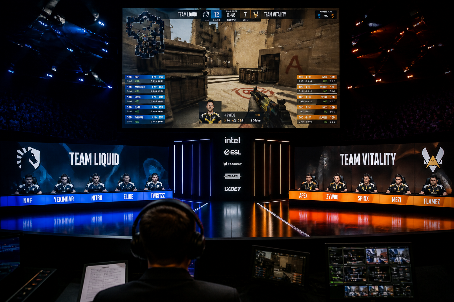 A wide shot of an esports tournament stage with two teams of players at their desks, with a large screen above showing the game.